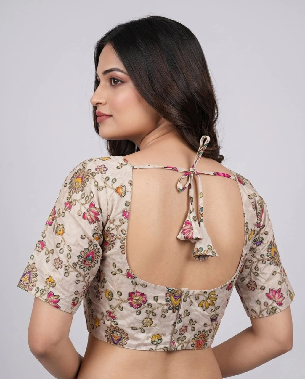 Woman wearing a floral blouse with an open back design on a plain background