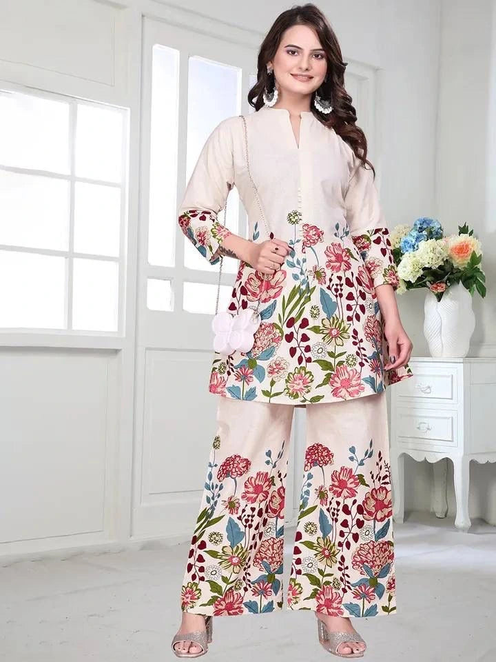 Woman wearing a floral outfit in a bright room with white walls and a vase of flowers.