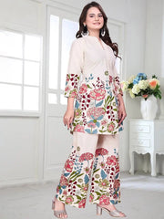 Woman wearing a floral dress in a bright room with a vase of flowers on a table.