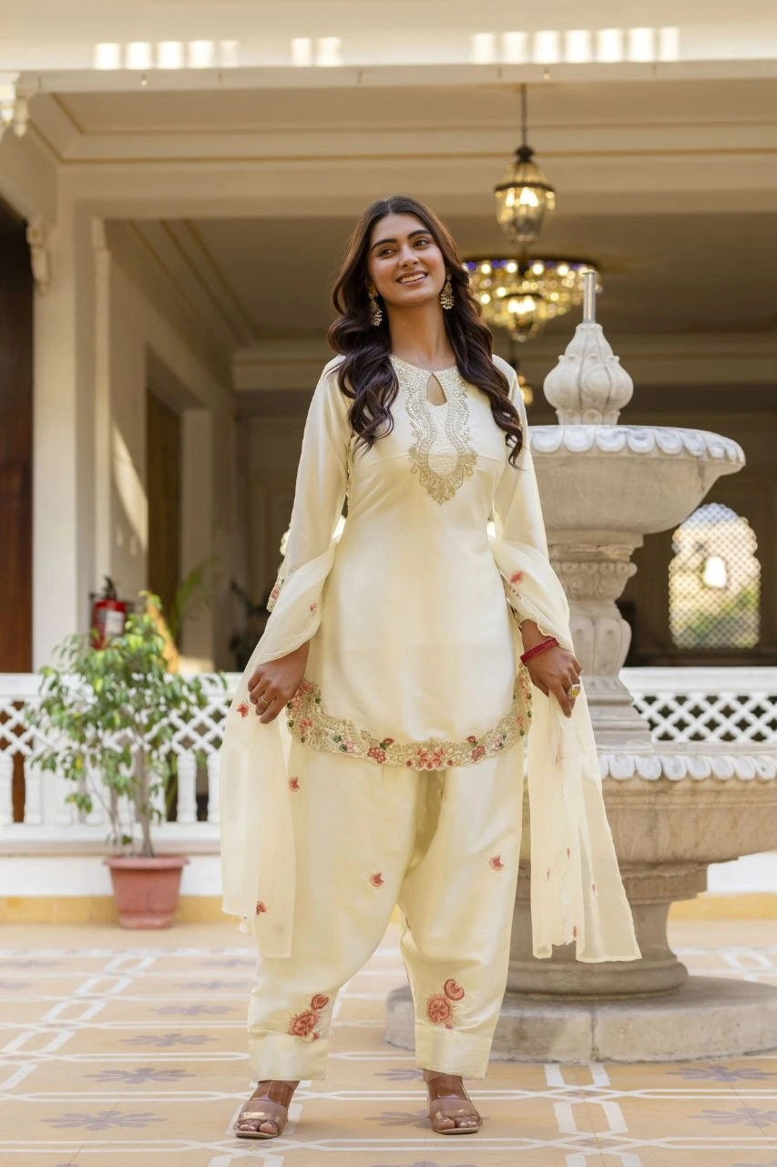 Woman in a cream traditional outfit standing in an elegant indoor setting with a fountain.