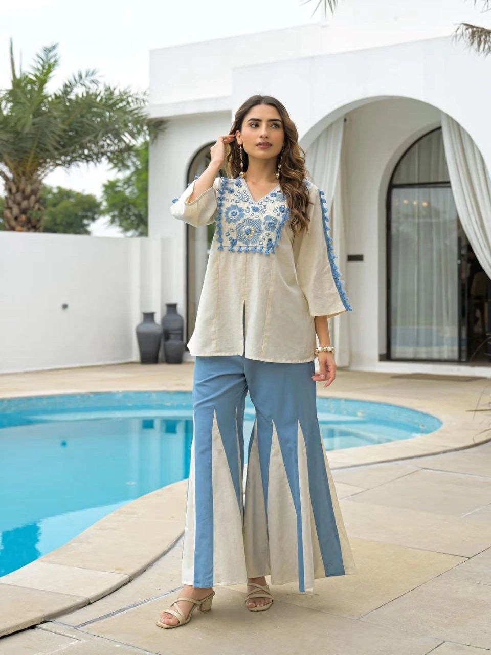 Woman in a beige and blue outfit standing by a poolside.