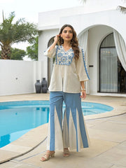 Woman in a beige and blue outfit standing by a poolside.