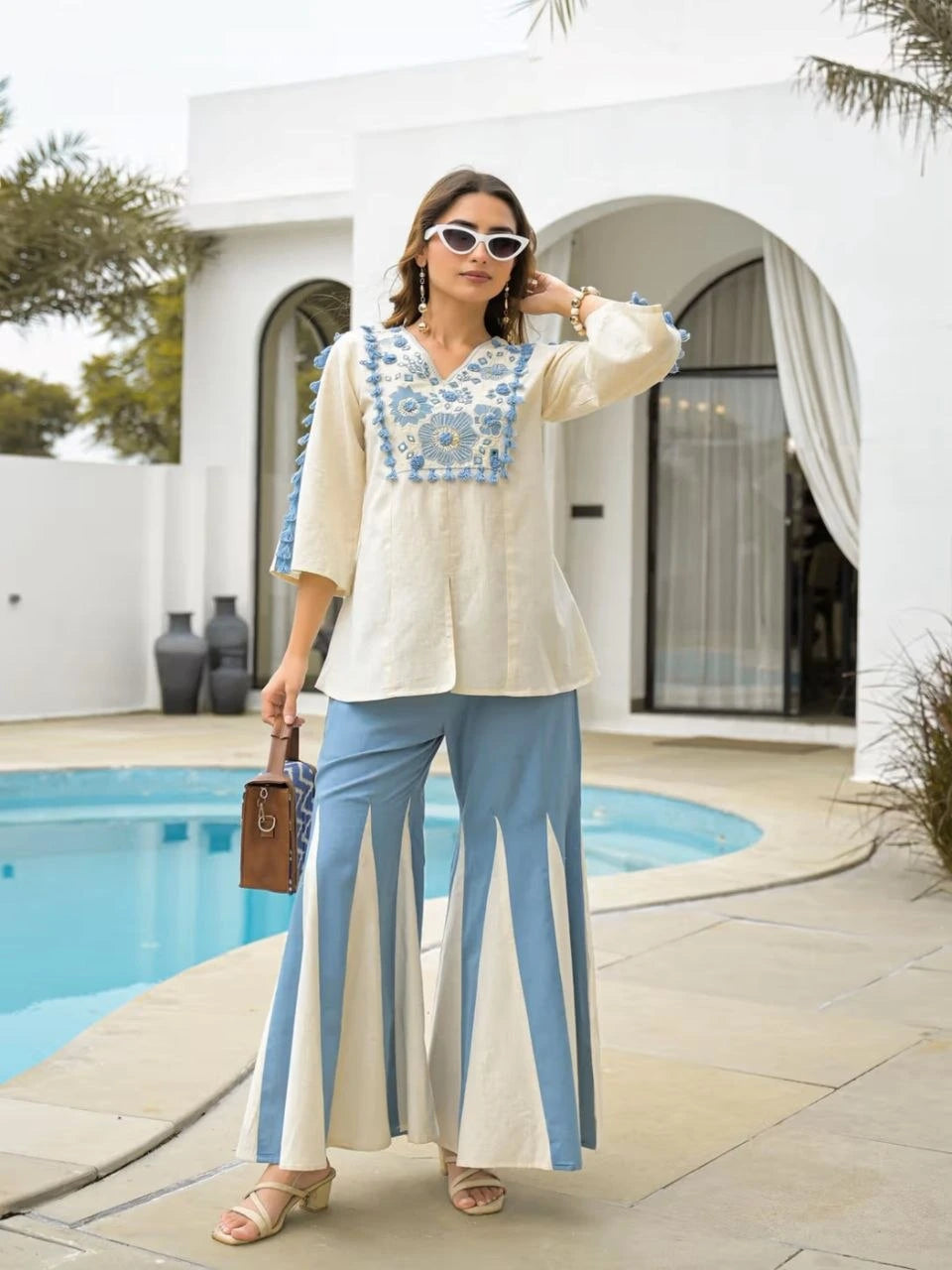 Woman in a white and blue outfit standing by a poolside.
