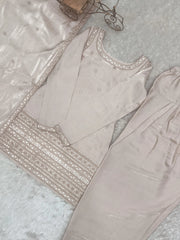 Light gray traditional outfit with intricate embroidery on a textured surface