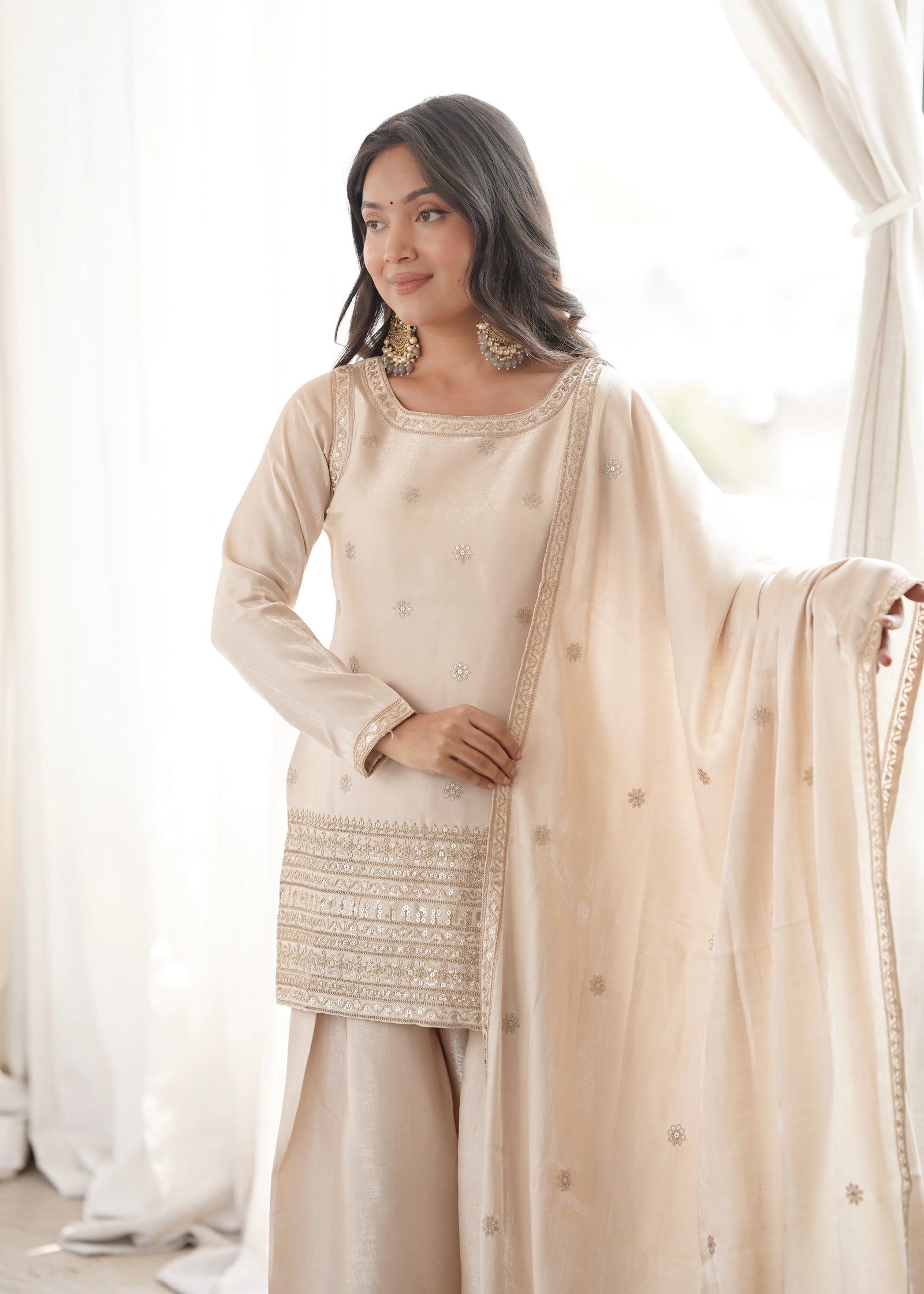 Woman wearing a traditional outfit with a beige top and skirt, holding a matching dupatta.