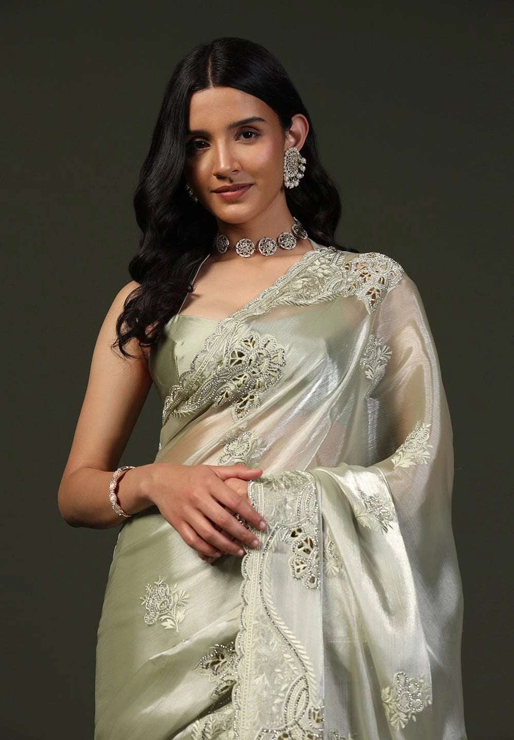 Woman wearing a light green saree with intricate patterns against a dark background
