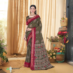Woman in an olive green sequence jacquard work saree with red border standing indoors against a backdrop of beige curtains and floral woven decor elements