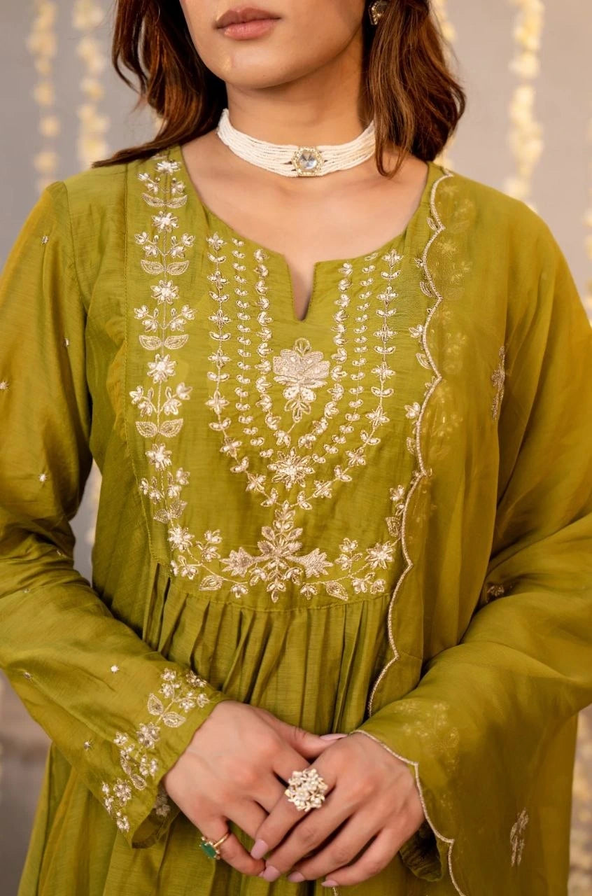 Green embroidered dress with white details worn by a person, against a neutral background.