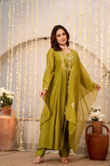 Woman in a green traditional outfit standing in front of decorative string lights and vases.