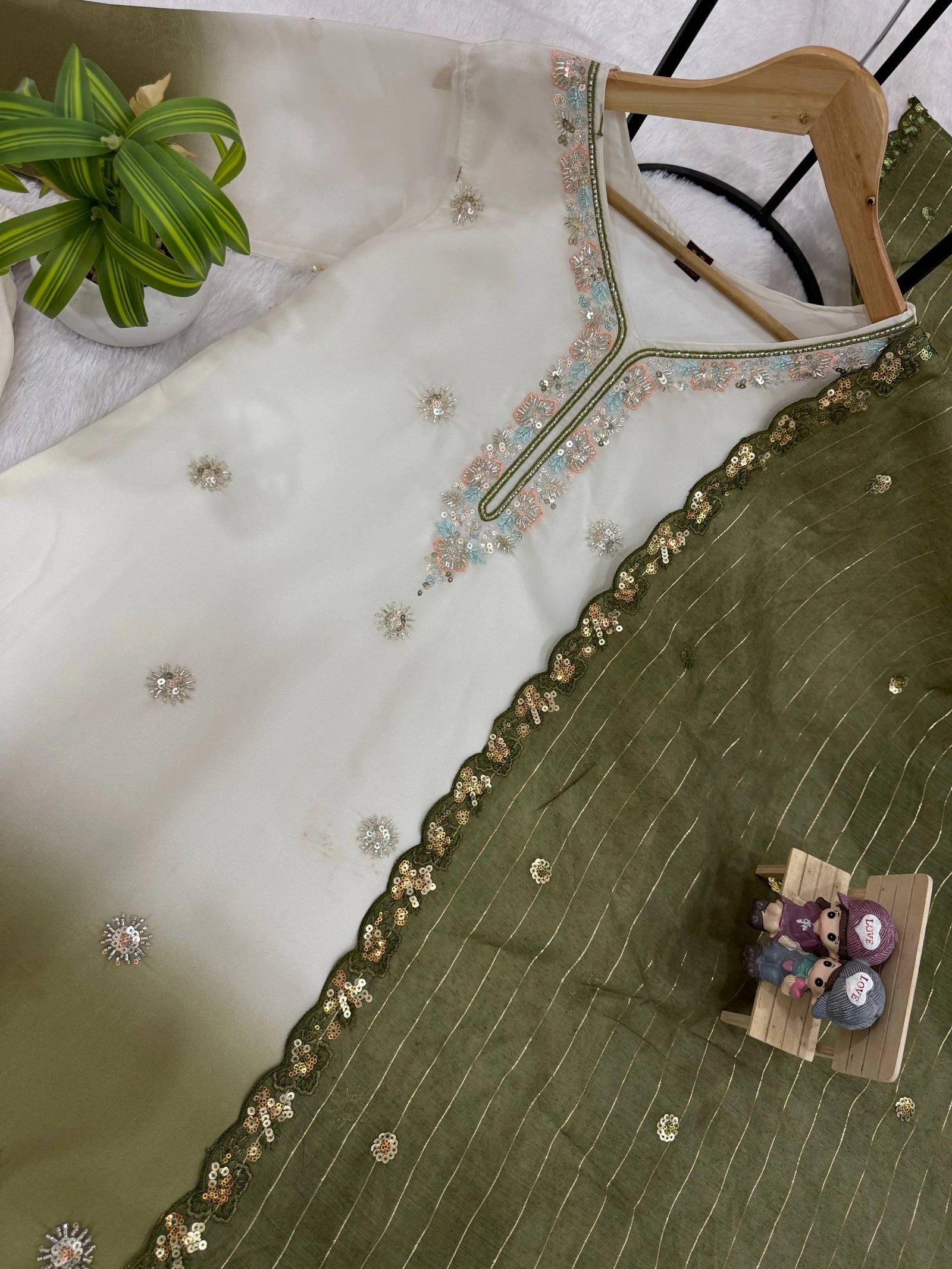 Green embroidered garment on a hanger with a small model of a family sitting on a box.