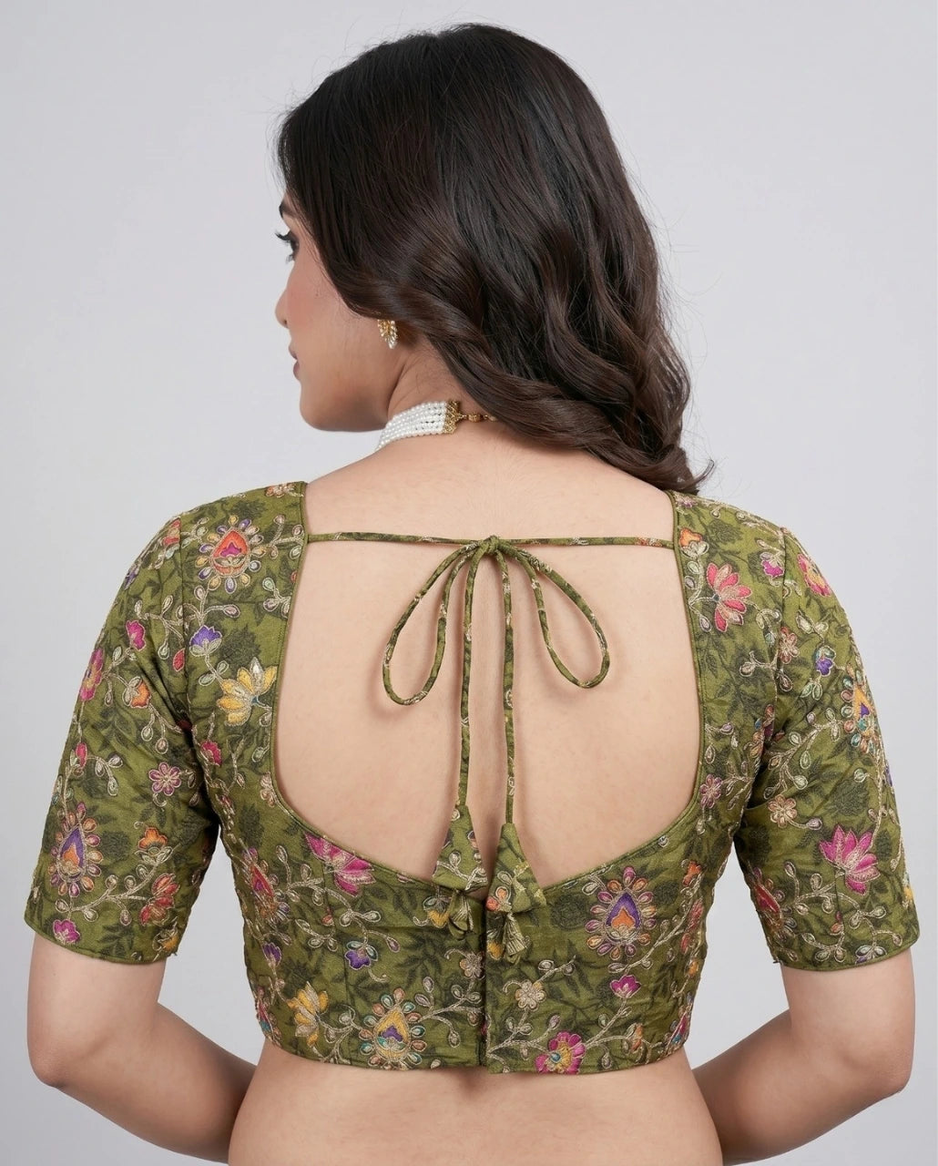 Woman wearing a green floral blouse with an open back on a plain background