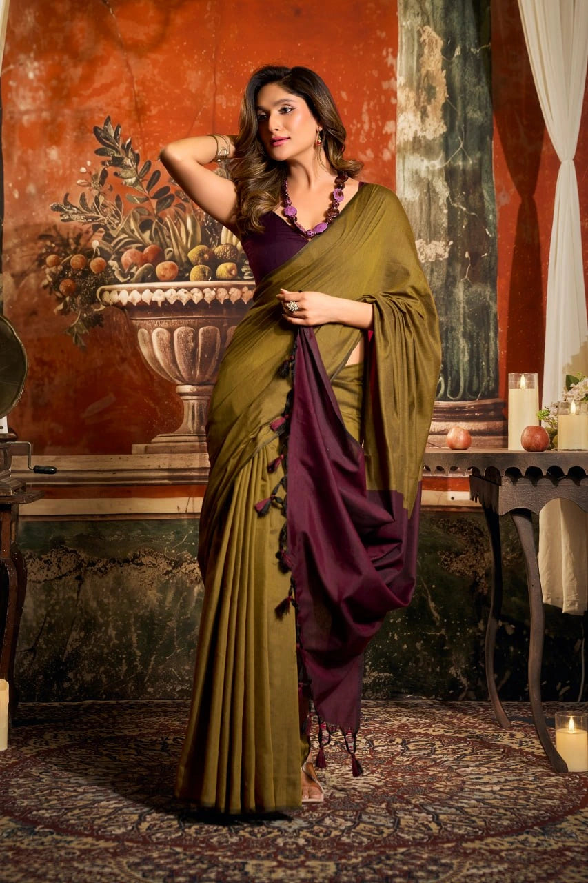 Woman in a green and purple saree standing in an ornate room with classical decor.