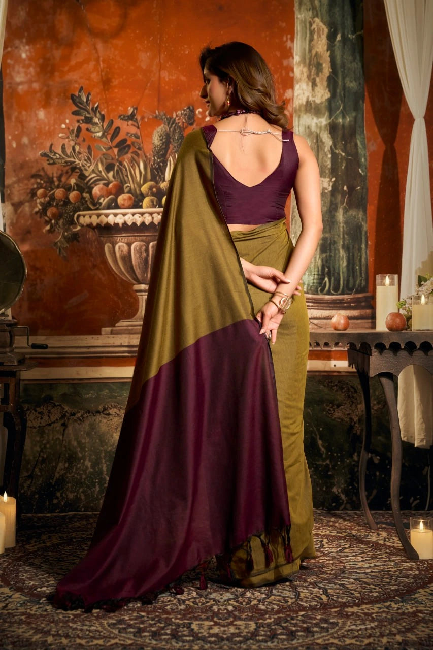 Woman in a green and purple saree standing in a decorated room with candles and a vase.