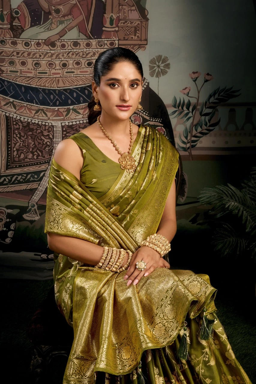 Woman in a green saree with gold jewelry against an ornate wall.