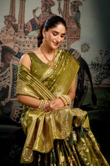 Woman in a green saree with gold jewelry against a decorative wall.