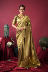 Woman in a gold saree standing against a red background with decorative items.