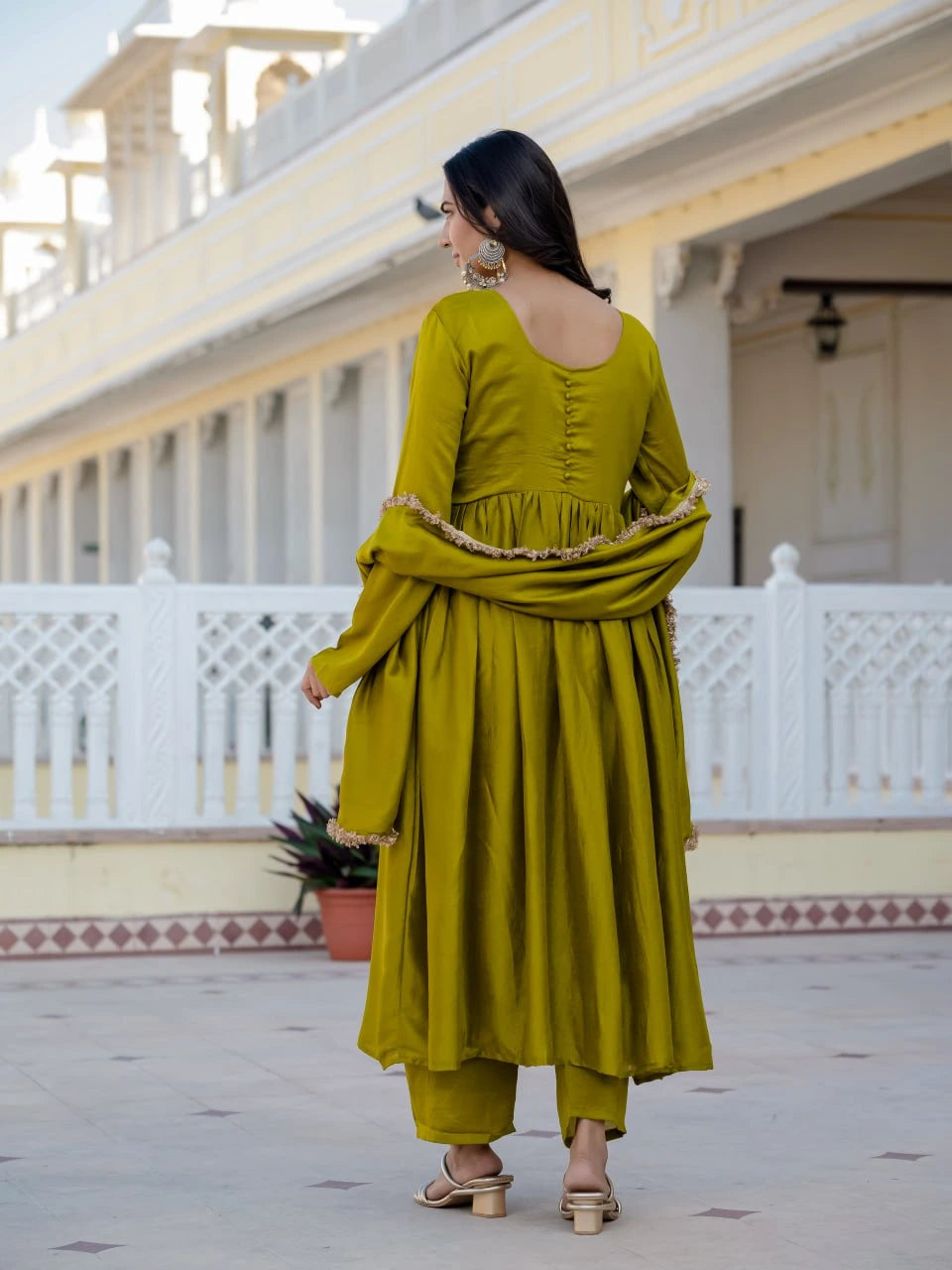 Woman in a green traditional outfit standing in front of a white building with columns.