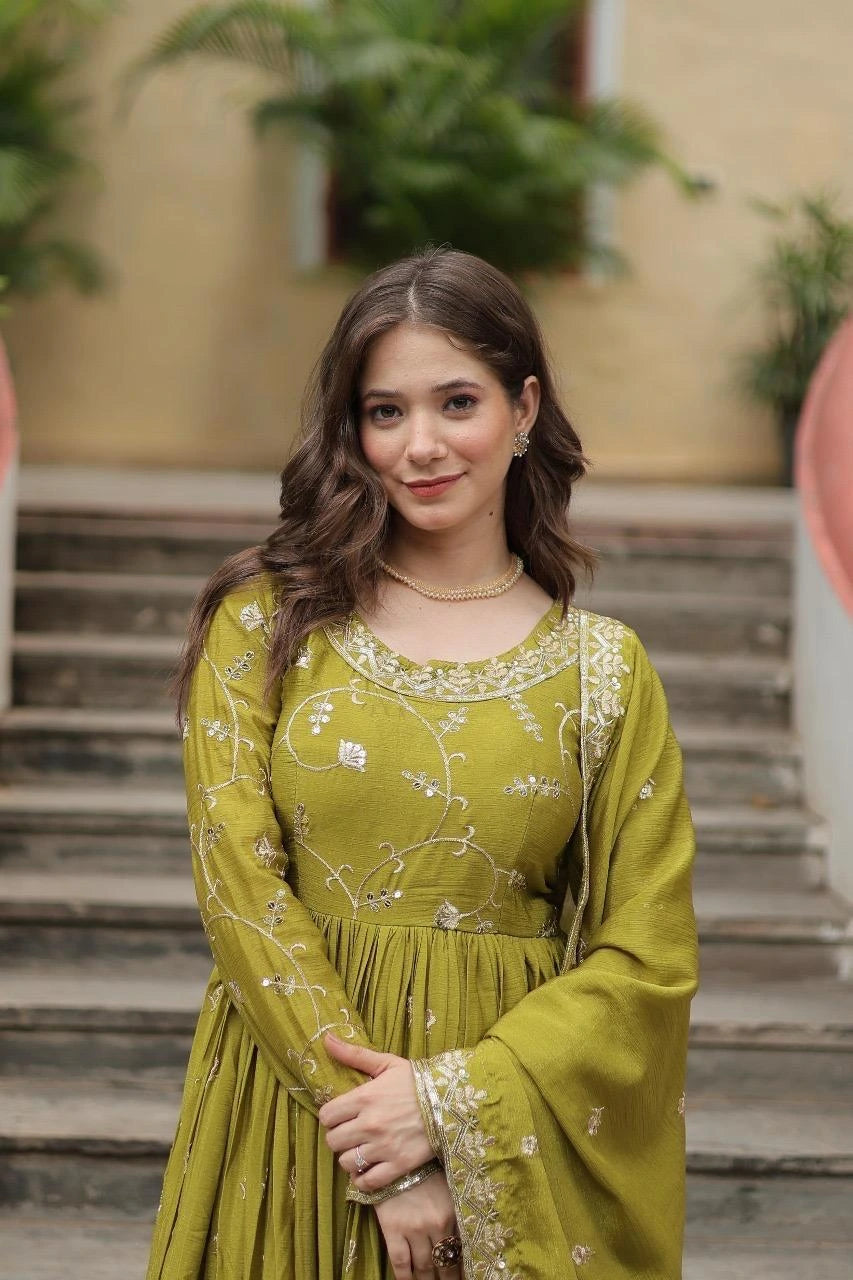 Woman in a green traditional outfit standing outdoors with plants in the background