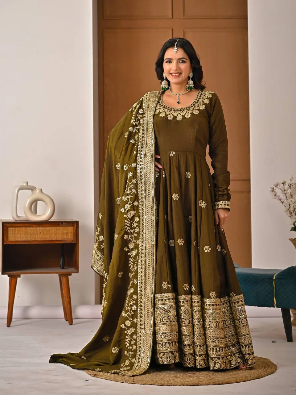 Woman wearing a traditional brown and green embroidered outfit in a room setting.