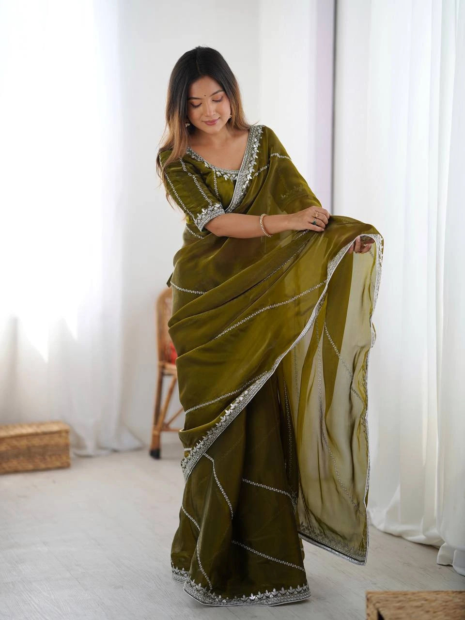 Woman wearing a green saree with white border in a minimalistic room.