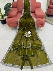 Green fabric with white lace trim on a white surface, with a pink sofa and plant in the background.