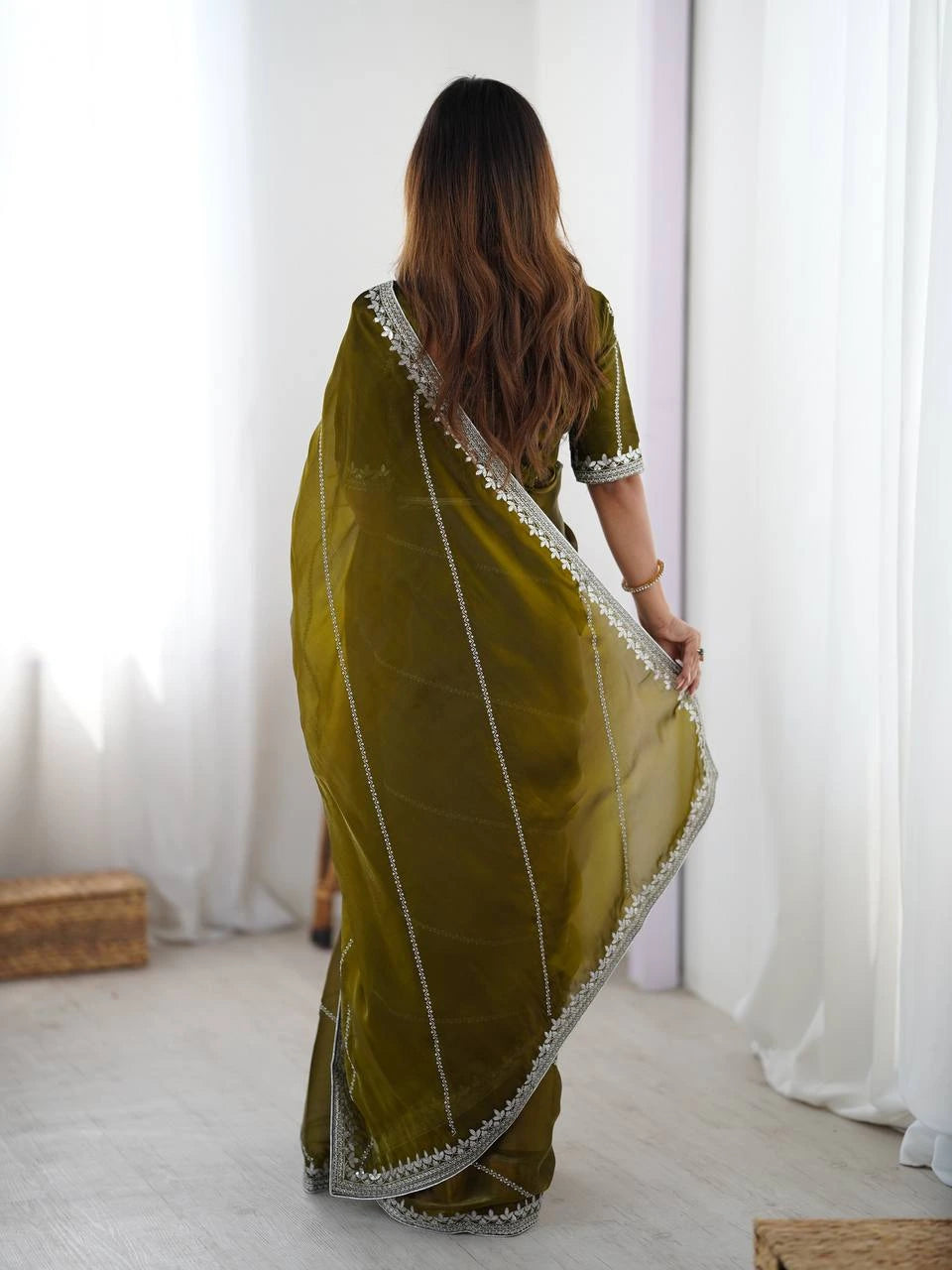 Woman wearing a green saree with white border in a minimal indoor setting