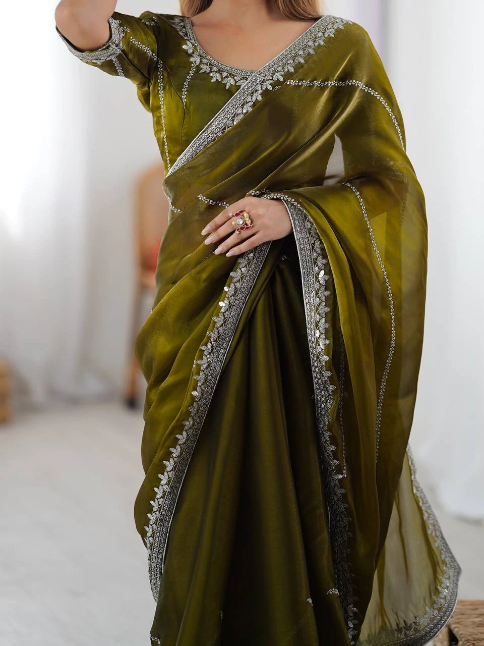 Green saree with silver border being held by a person against a white background