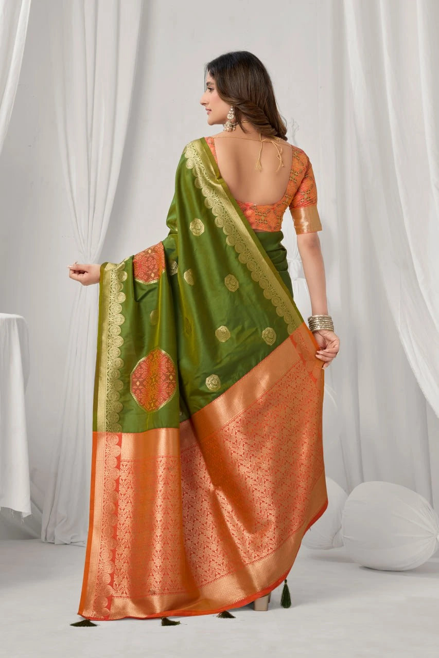 Woman wearing a green and orange saree with a white curtain background