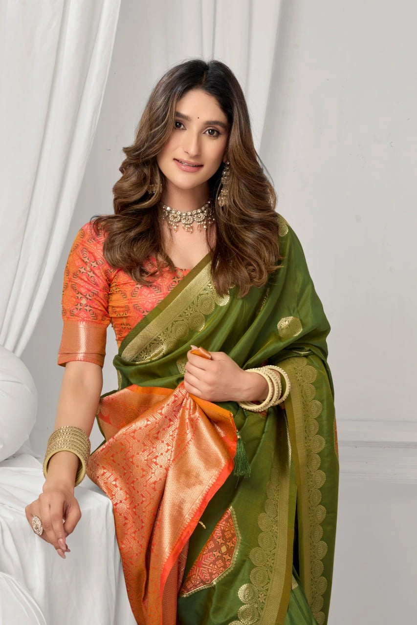 Woman wearing a green and orange saree with a white curtain background
