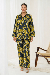 Woman wearing a black and yellow floral outfit standing in a room with a chair.