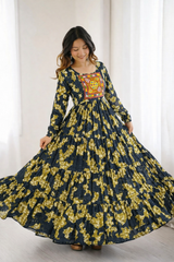 Woman wearing a long floral dress with a colorful patterned top against a white curtain background