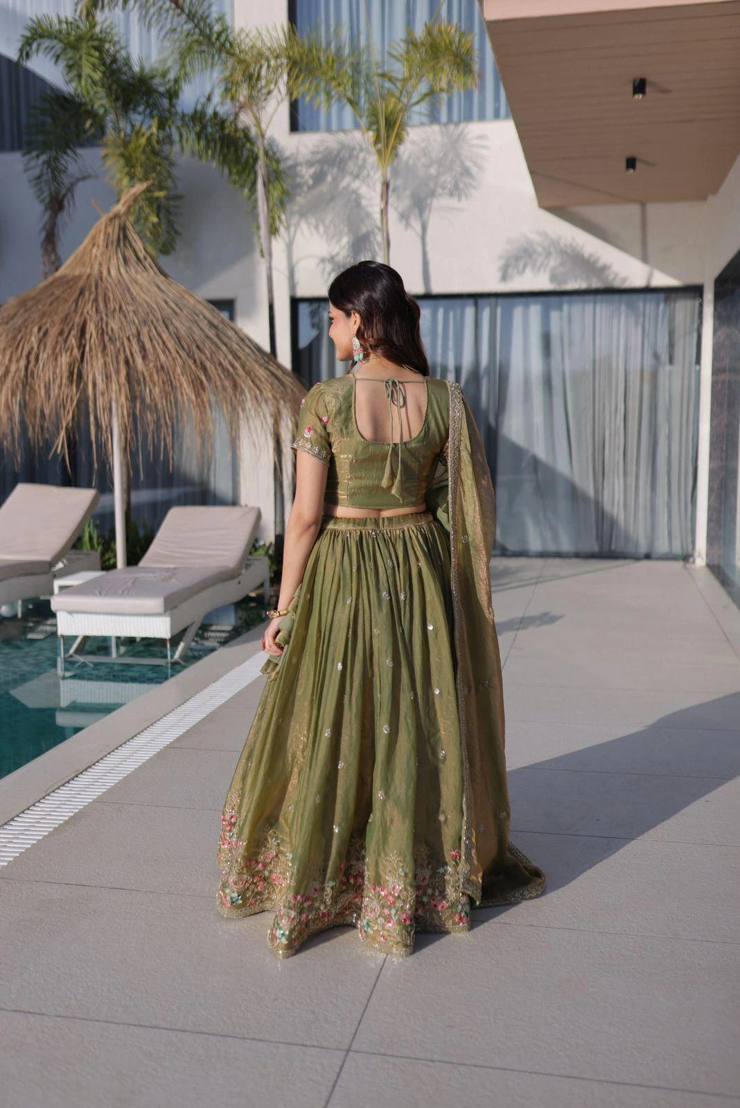 Woman in a green traditional outfit standing by a poolside with modern architecture in the background