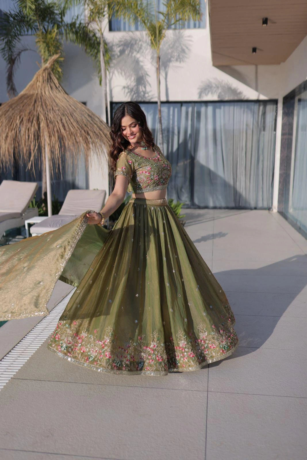 Woman in a green embroidered traditional outfit standing outdoors with modern architecture in the background