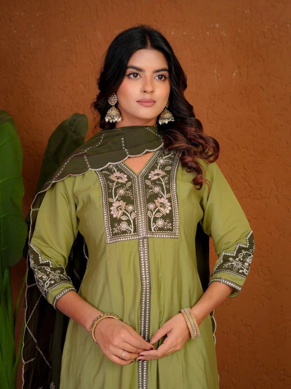 Woman wearing a green embroidered traditional outfit against an orange background