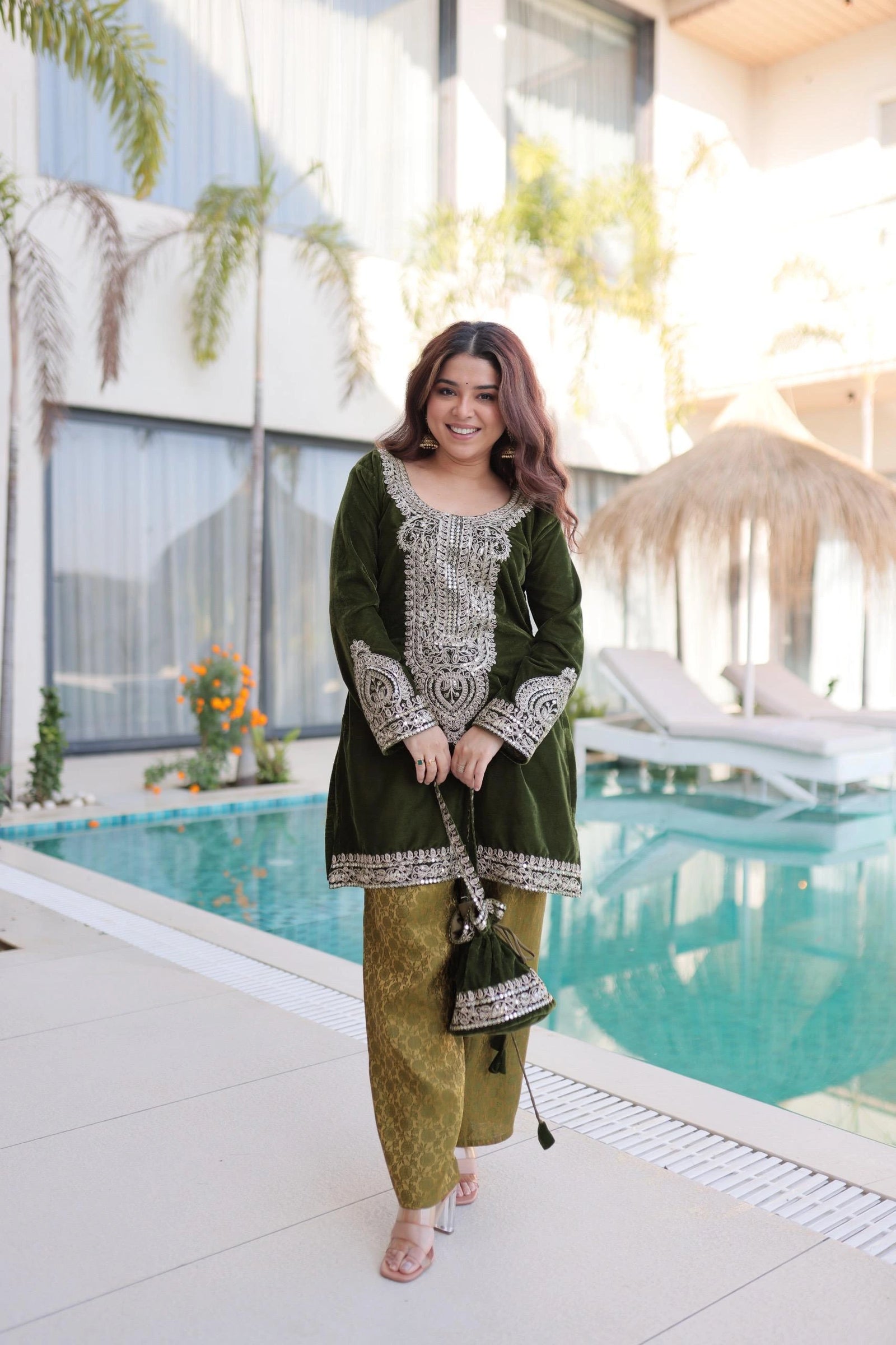 Woman in a green traditional outfit standing by a poolside.