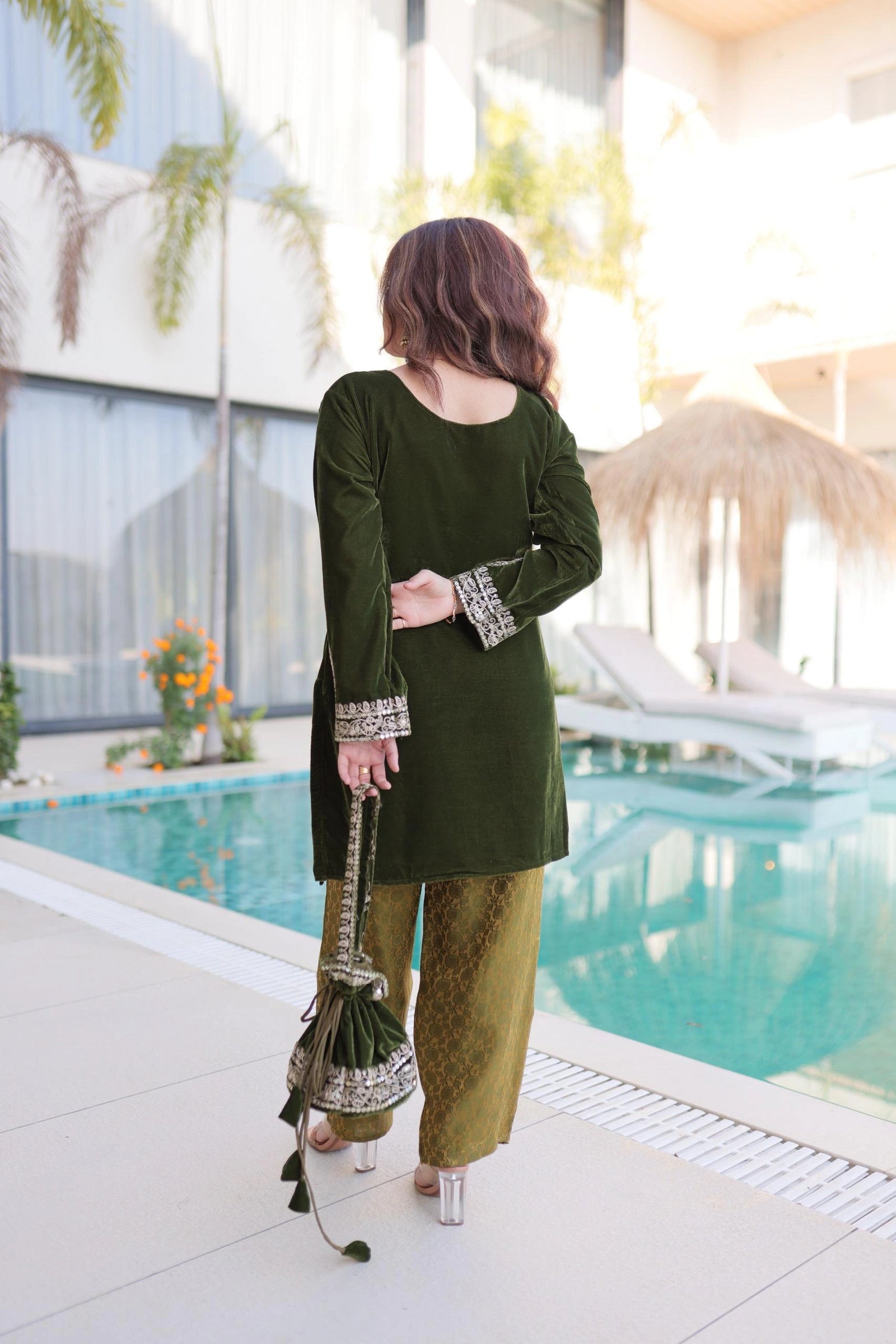 Woman in green traditional outfit standing by a poolside