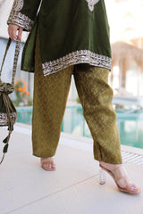 Person wearing a green outfit with patterned pants and a matching top, holding a handbag.