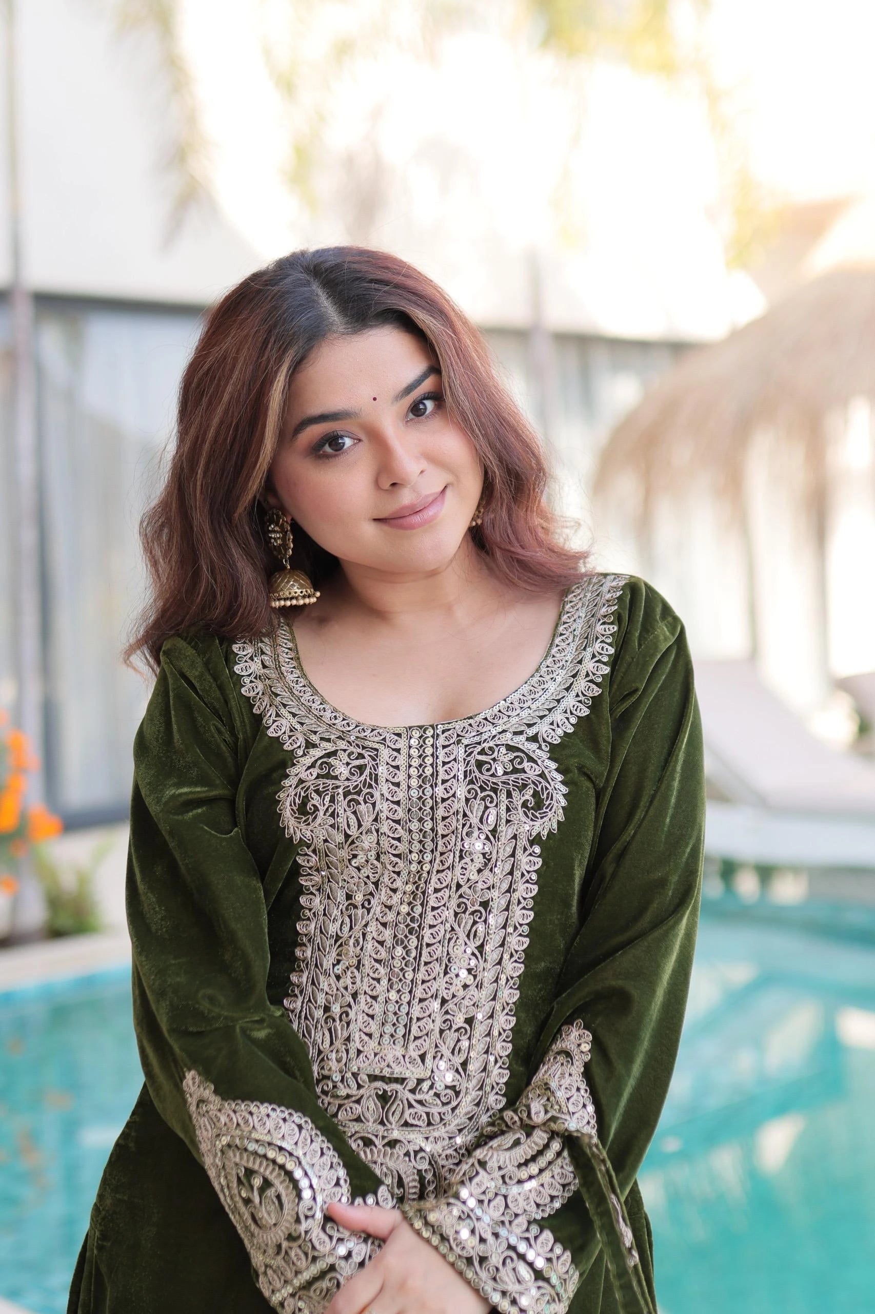 Woman in a green traditional outfit with intricate white embroidery by a pool