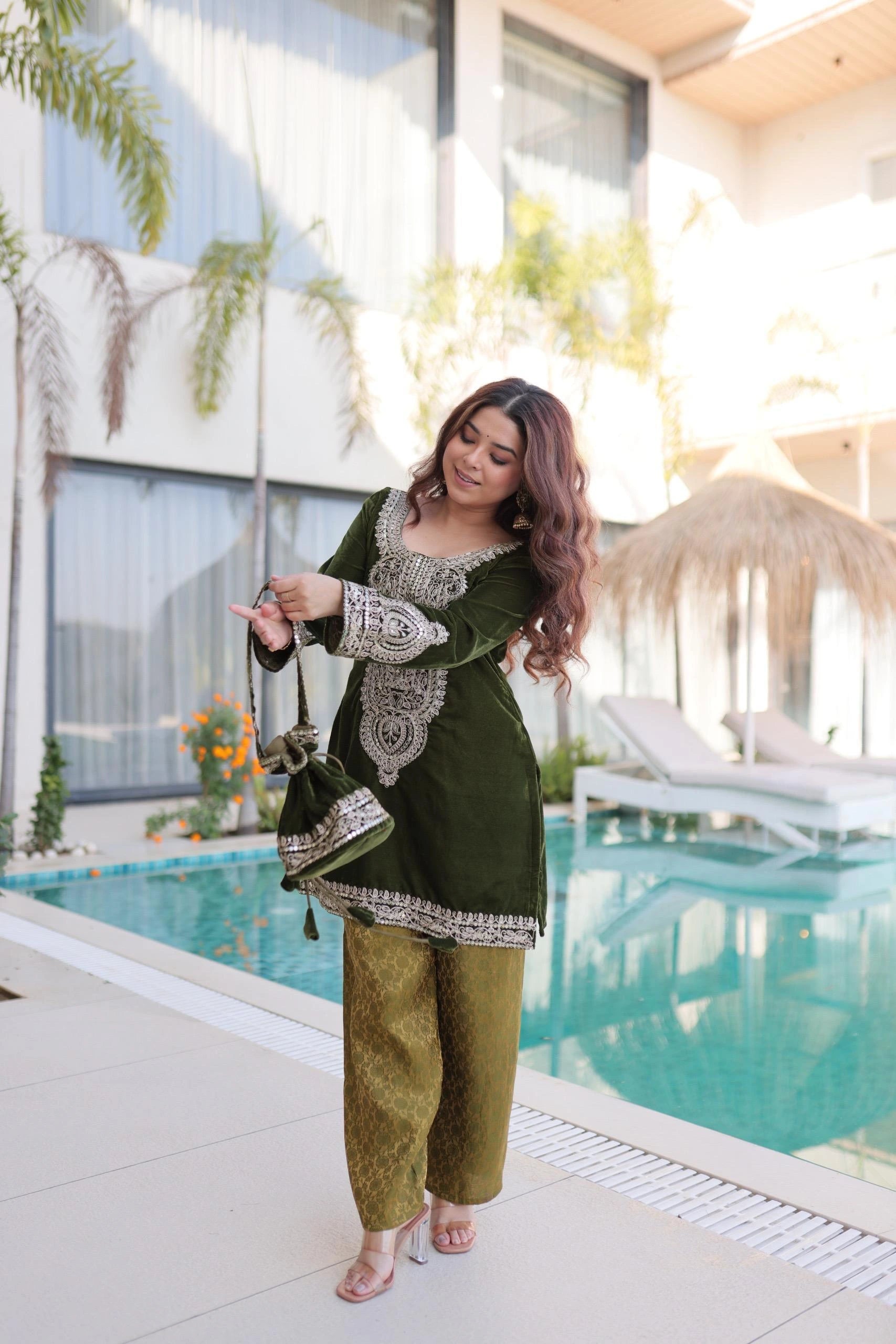 Woman in a green outfit standing by a pool with a modern building and plants in the background