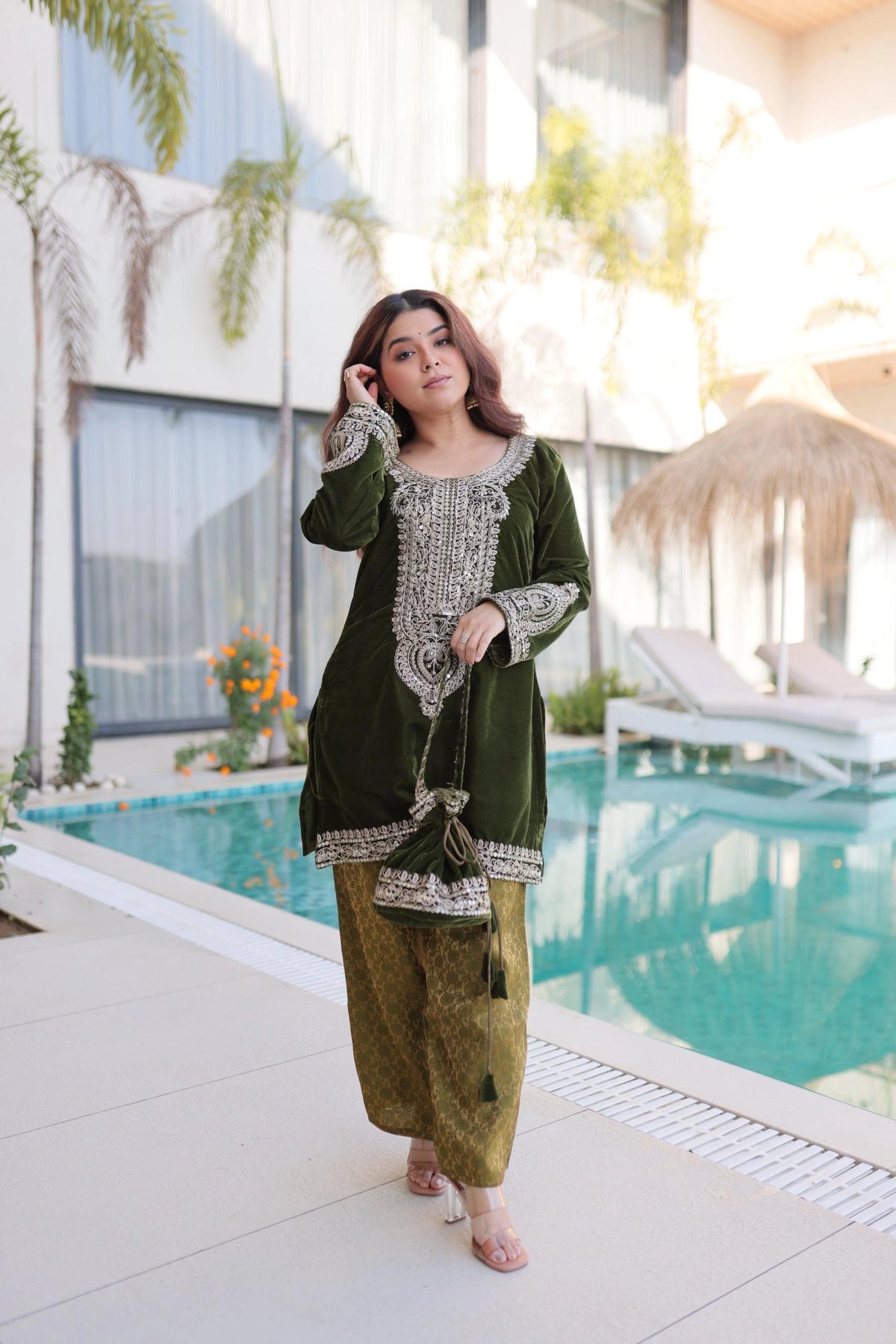 Woman in a green traditional outfit standing by a poolside.