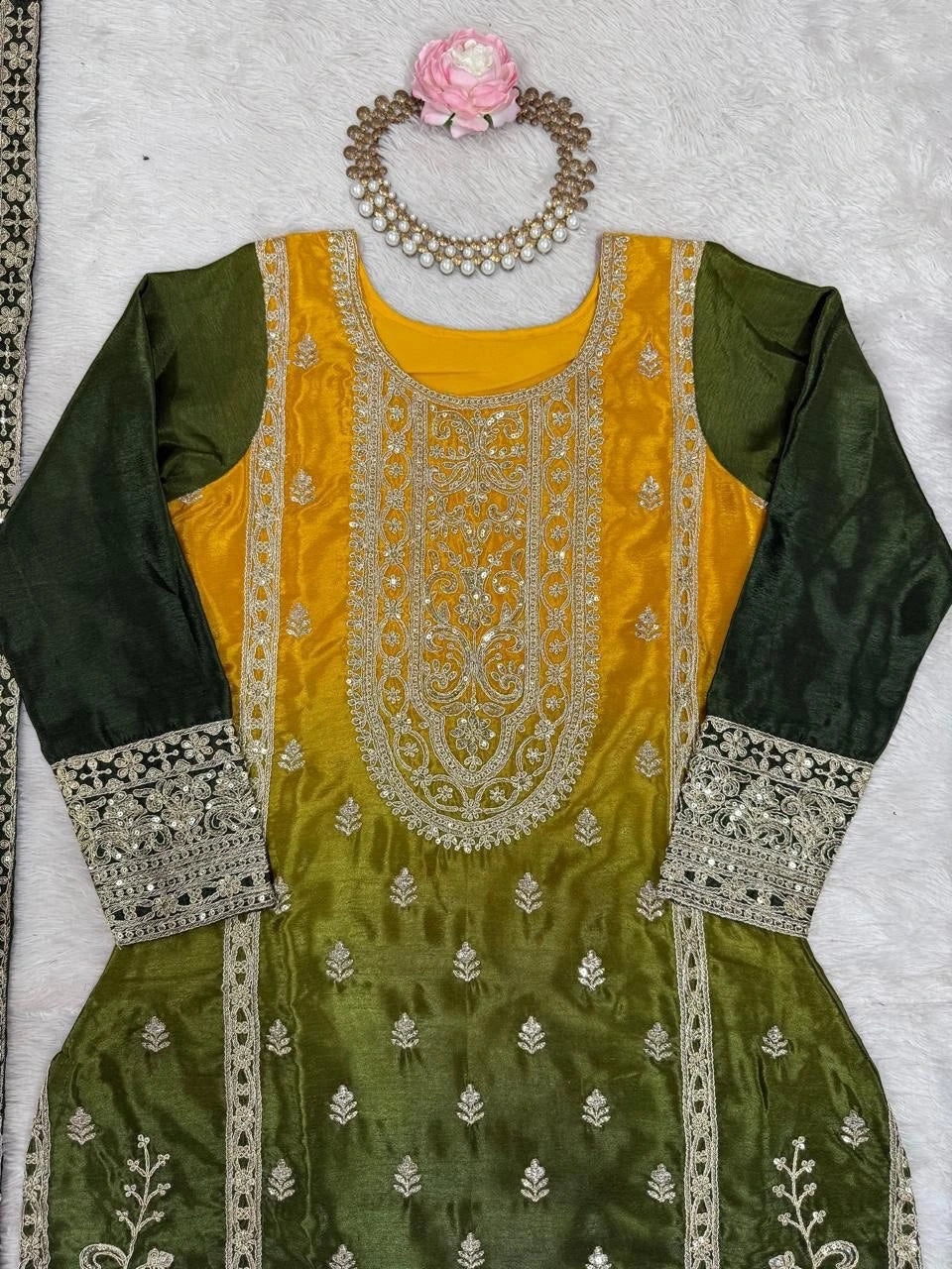 Green and yellow embroidered traditional outfit with jewelry on a light gray background