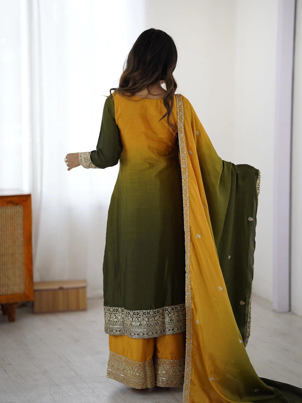 Woman wearing a green and yellow traditional outfit with a matching dupatta in a minimal indoor setting.