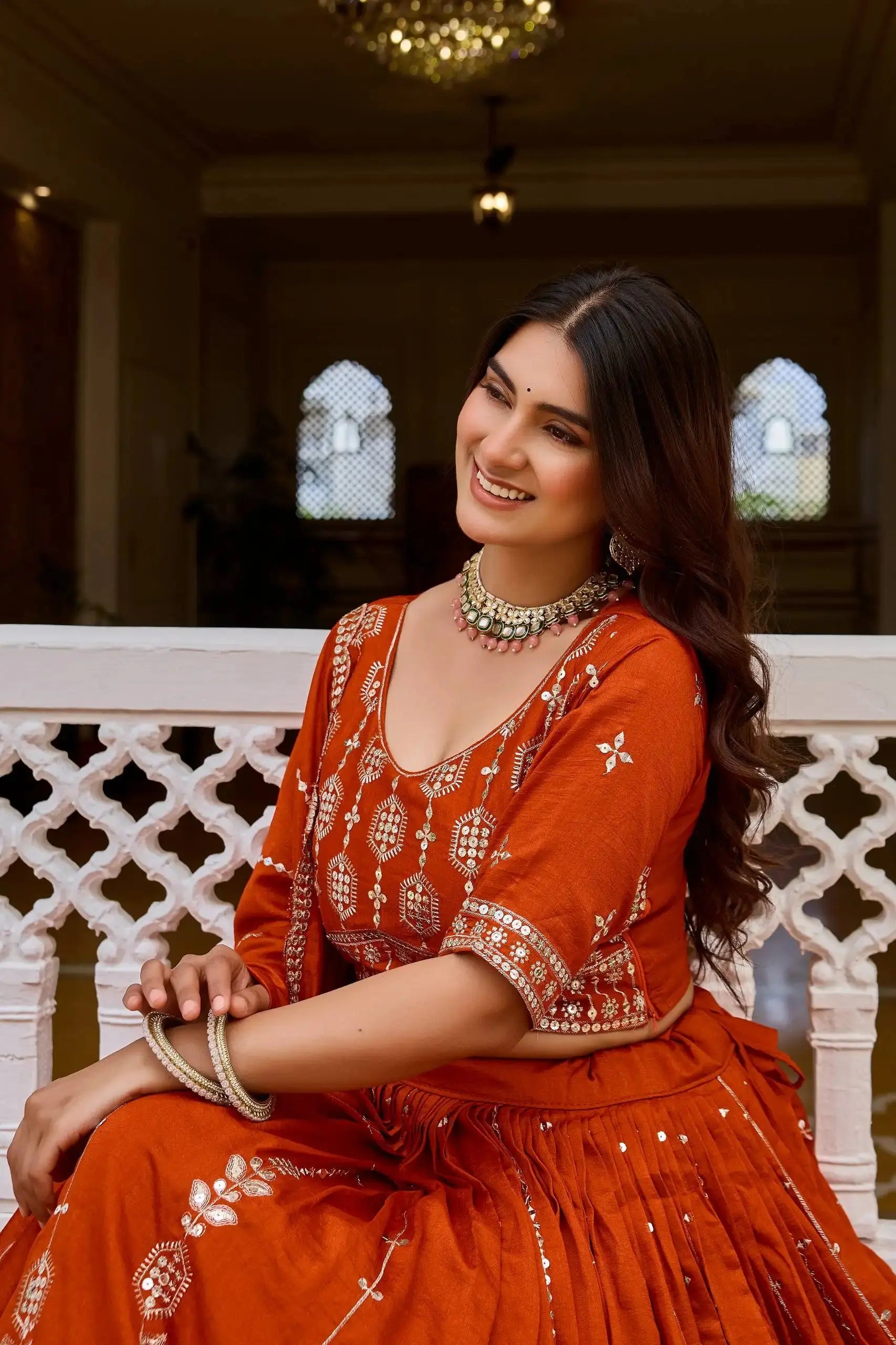 Portrait of model in orange sequins embroidered lehenga showing choli embroidery detail