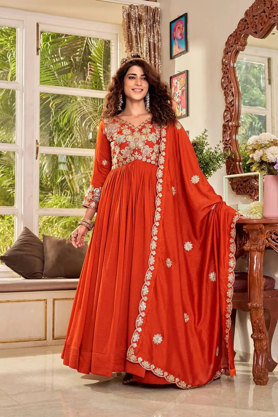 Woman in a red traditional outfit with floral patterns standing in a room with a window and decor.