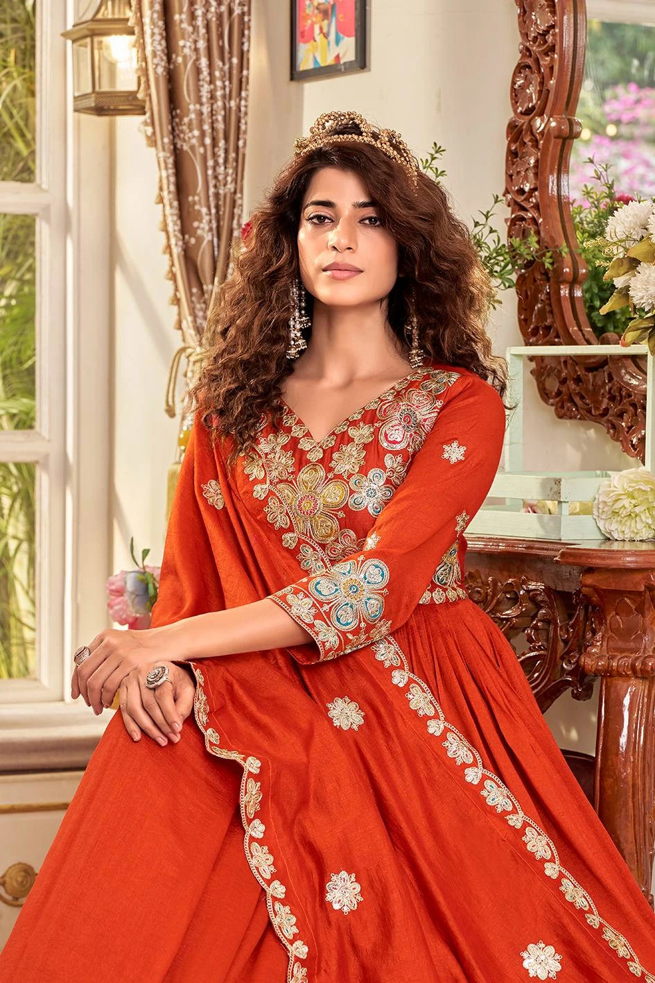 Woman in a red embroidered traditional outfit sitting in a decorated room.
