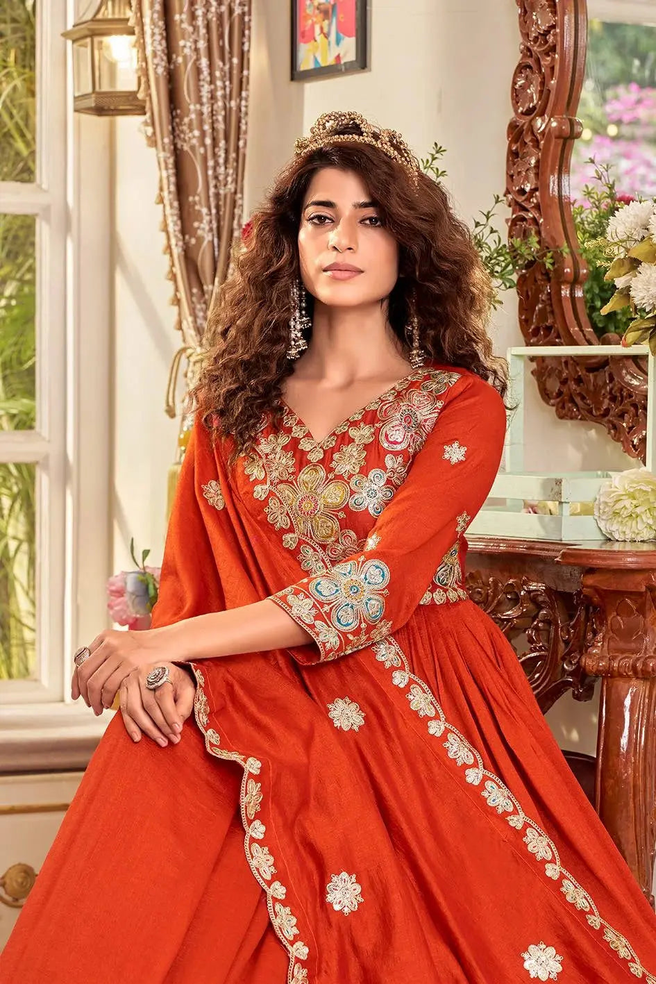 Woman in a red embroidered traditional outfit sitting in a decorated room.