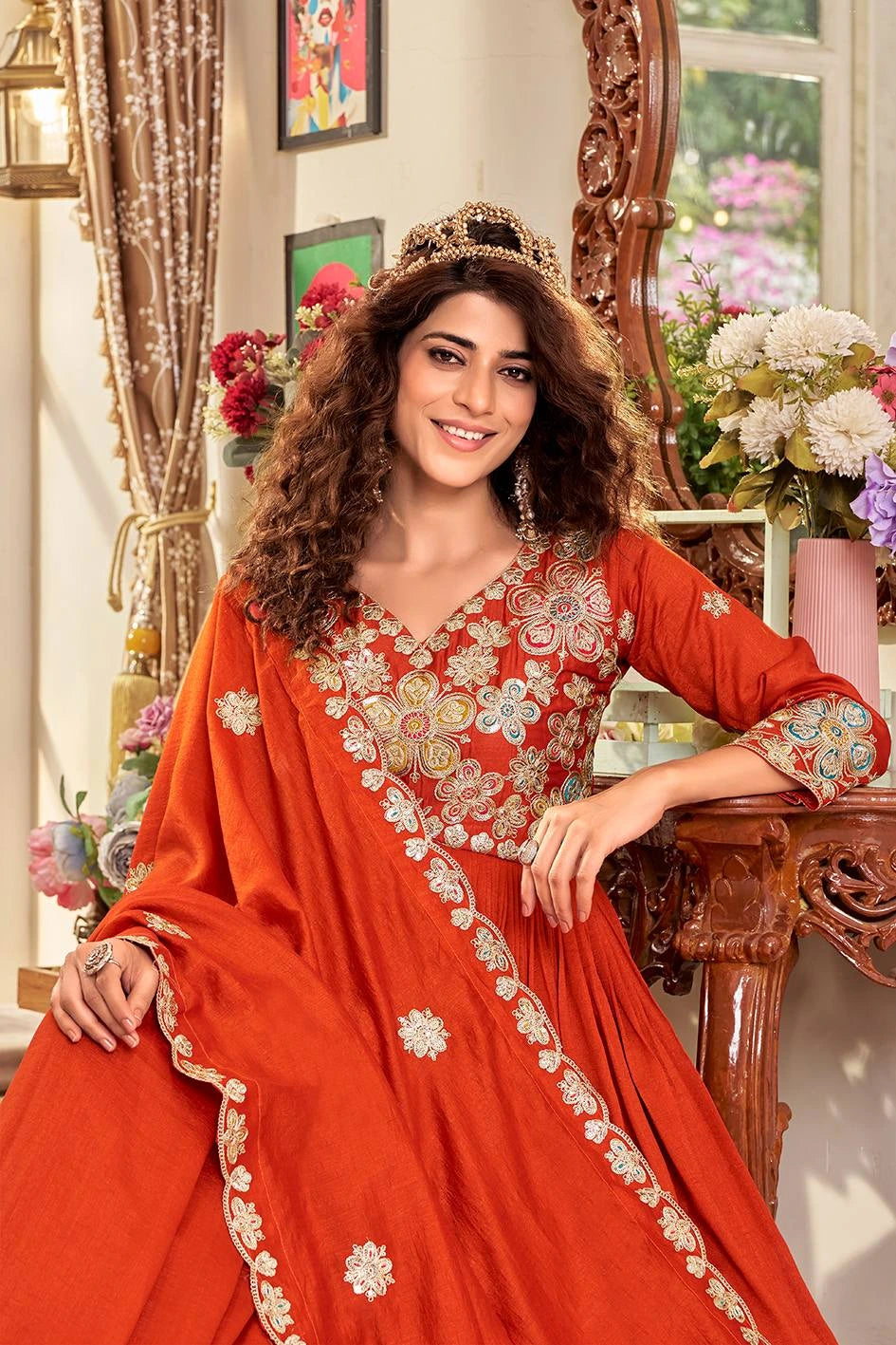 Woman in a red embroidered traditional outfit sitting in a decorated room.