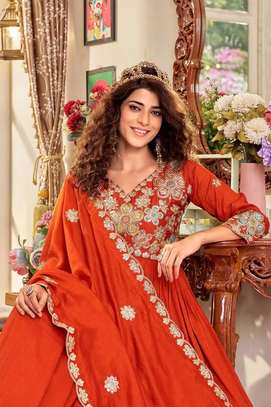 Woman in a red embroidered traditional outfit sitting in a decorated room.