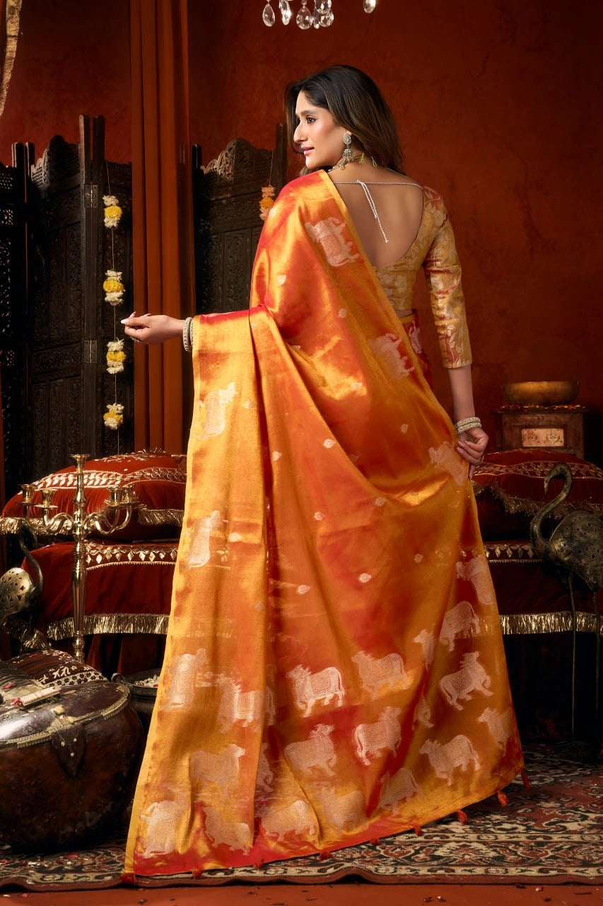 Woman in an orange saree with elephant patterns in a decorated room.