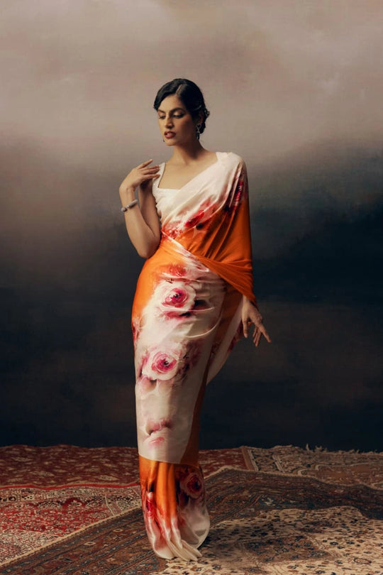 Woman wearing a floral saree with an orange border against a dark background